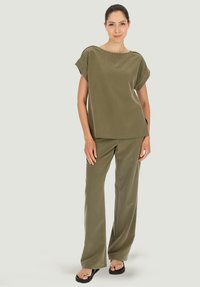 Oliwkowy, luźno dopasowany top z podwiniętymi rękawami oraz pasującymi, wysokim stanem spodniami o szerokich nogawkach; gładka tkanina o miękkiej strukturze.