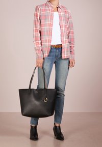 Svart läder tote-väska med en texturerad yta och ett guldtonat detaljer. Kombineras med en rosa rutiga skjorta och blå jeans.