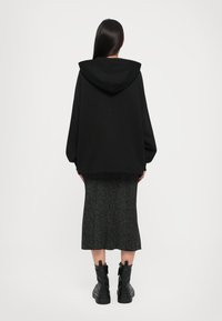 Hoodie oversized preto com capuz, combinado com uma saia de malha cinza até ao joelho, e botas de combate pretas com solas grossas.