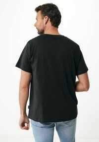 �Černé tričko s krátkým rukávem, volnější střih, s kulatým výstřihem. Měkký bavlněný materiál; malá etiketa na levé spodní straně. Nenošeno s světlými modrými džínami.