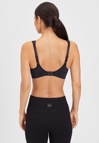 Sort sportsbh med justerbare stropper, glat tekstur og hægte-lukning bagpå, parret med højtaljede sorte leggings.
