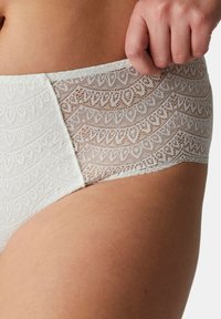 Weiße Spitzenunterwäsche mit einem gemusterten Design, gewellten Kanten und einem glatten Bund. Der Stoff ist semitransparent mit einer zarten Textur.