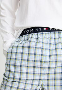 Bokso šortai su mėlynu, geltonu ir baltu akiniu raštu; turi juodą juosmenį su "TOMMY HILFIGER" užrašu. Atsipalaidavęs siluetas.