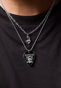 Dos collares de plata de dos capas: uno con un charm de escorpión y el otro con un colgante de pua de guitarra negra con texto y diseño gráfico en blanco.