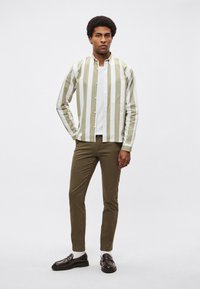 Gestreept overhemd met knopen in lichtgroen en wit, met een zak; gecombineerd met olijfgroene broek en zwarte leren schoenen.