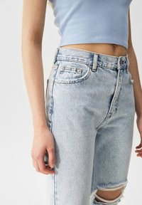 Top corto acanalado azul claro combinado con unos jeans de tiro alto en un tono azul desgastado, con una rodillera rasgada y un diseño clásico de cinco bolsillos.