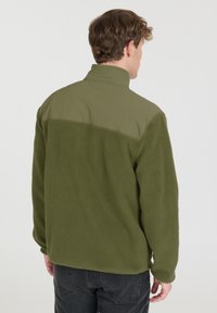 Grüne Fleecejacke mit einem glatten, olivgrünen oberen Abschnitt. Verfügt über einen hohen Kragen und eine strukturierte Oberfläche, geeignet für die Freizeit.