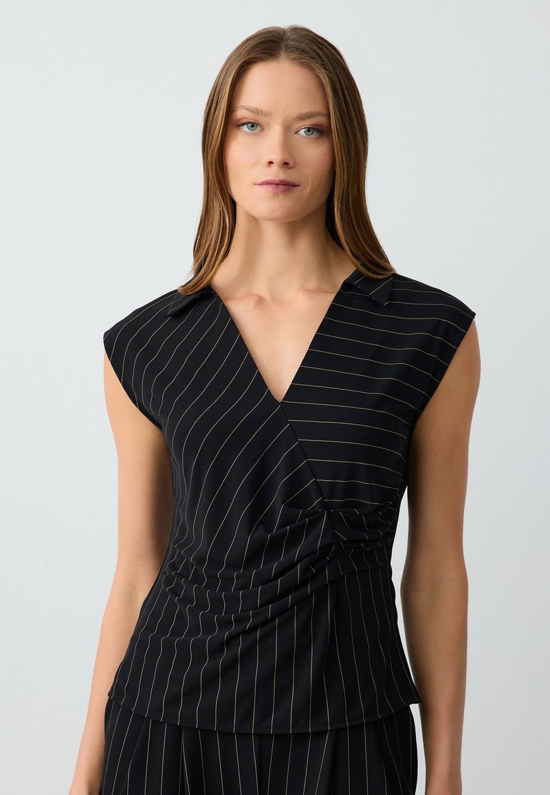 Maglietta nera con strisce verticali dorate, maniche corte a cappuccio, scollatura a V e un design frontale attorcigliato per aggiungere texture e forma.