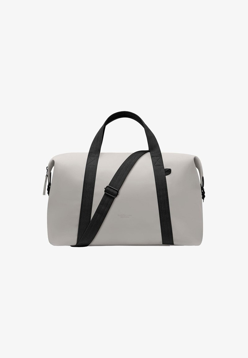 Bolsa de lona en gris claro con asas de cinta negra y correa ajustable. Cuenta con un cierre de cremallera y un detalle sutil del logo.