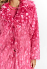 Cappotto in pelliccia sintetica di un brillante colore rosa con macchie bianche, dotato di colletto, bottoni e maniche lunghe. La morbidezza del tessuto esalta il design vivace.
