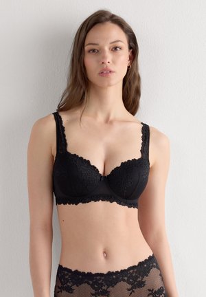 Černá krajková podprsenka s vycpávanými košíčky, vroubkovanými detaily a nastavitelnými ramínky. Obsahuje květinové vzory a hladký spodní pás pro podporu.