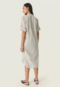 Robe midi rayée en tissu léger, dotée de manches courtes retroussées, d'une taille cintrée et de fentes latérales. Les couleurs sont crème avec des rayures marines.