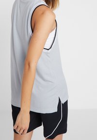Szary sportowy top bez rękawów z bocznymi rozcięciami, ozdobiony czarno-białą lamówką. Do kompletu czarne szorty z białymi akcentami.