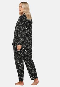 Conjunto de pijama negro con patrones abstractos blancos, que incluye una camiseta de manga larga y pantalones holgados. Hecho de una tela suave y ligera.