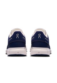 Baskets de course navy avec tige en mesh, semelles blanches et détails réfléchissants à l'arrière. Présente un talon rond et un marquage minimal.