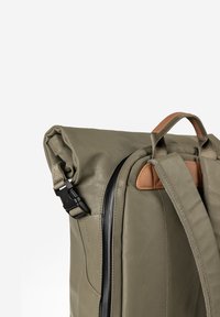 Olive green roll-top backpack with black buckle, padded straps, brown leather details, and a vertical zipper on the back panel.