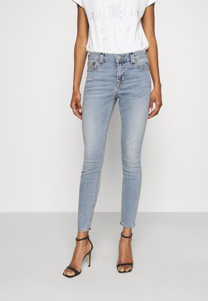 Kvinde iført lyseblå skinny jeans og sorte højhælede sandaler, kombineret med en hvid top med korte ærmer.