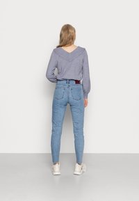 Top gris de manga larga con escote en V, combinado con jeans ajustados de color azul claro y zapatillas beige. Diseño simple sin patrones.
