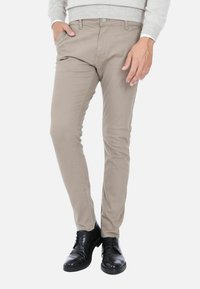 Pantaloni beige slim-fit con una trama liscia, dotati di tasche laterali e vita con bottone, abbinati a scarpe in pelle nere.