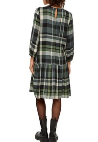 Grünes und schwarzes karierter Kleid mit langen Puffärmel, gerafftem Rock und Rückenschlitz. Der Stoff wirkt leicht und strukturiert.