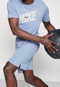 Camiseta Nike de color azul claro con un gran logo blanco, combinada con pantalones cortos a juego que tienen una abertura lateral, y una pelota de ejercicio negra texturada.