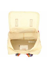 Plátěná taška s béžovým vnitřkem, horním otvorem, červeným prošitím a rukojeťmi se duhovým pruhem. Podšívka je hladká s viditelnou etiketou.