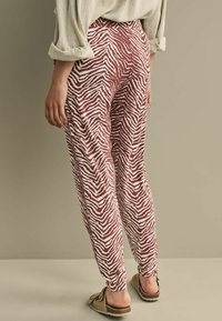 Røde og hvide zebra-stribede bukser med en afslappet pasform, elastisk talje og ankellængde, parret med lysebrune slip-on sko.