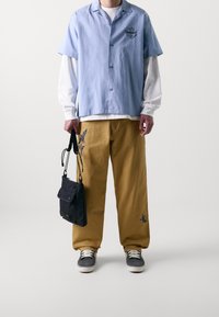 Vaaleansininen lyhythihainen paita, jossa logo, valkoinen pitkähihainen paita alla, vaaleanruskeat housut kirjailuin koristeltuna, musta laukku, harmaat tennarit.