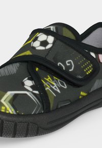 Chausson sombre pour enfant avec semelle noire, motif ballon de football et but, fermeture à scratch et détails accents jaunes.