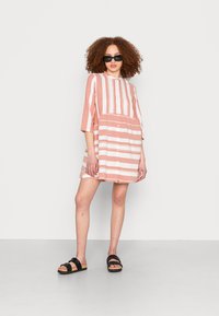Vestido listrado, de manga curta, em coral e branco, com um fecho de botões e design em camadas; combinado com sandálias pretas de tiras.
