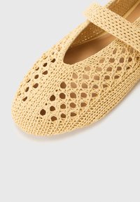 Scarpe piatte intrecciate gialle con punta chiusa e motivo a intaglio. Presentano una fascia larga sul collo del piede per il supporto.