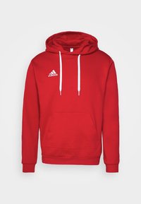 Sweat à capuche rouge Adidas avec cordons blancs, poche kangourou à l'avant et logo Adidas sur la poitrine gauche sur fond blanc uni.