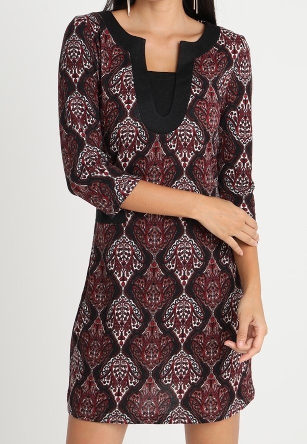 Femme portant une robe mi-longue avec un motif floral bordeaux, noir et blanc et des manches trois-quarts, avec un profond col noir en forme de U.