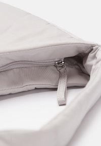 Il sacchetto di stoffa grigia presenta una chiusura con zip e un tirante metallico, oltre a una fodera interna. Il materiale morbido e strutturato esalta il suo design moderno.
