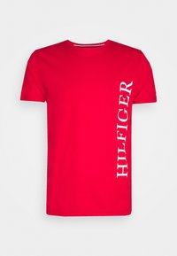 Červené bavlněné tričko s kulatým výstřihem, krátkými rukávy a vertikálním bílým nápisem "HILFIGER" na levé straně. Hladká textura.
