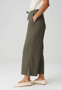 Lehký, olivově zelený, široký kalhoty s texturovanou tkaninou, páskem na šňůrku a bočními kapsami. V kombinaci s béžovými balerínami.