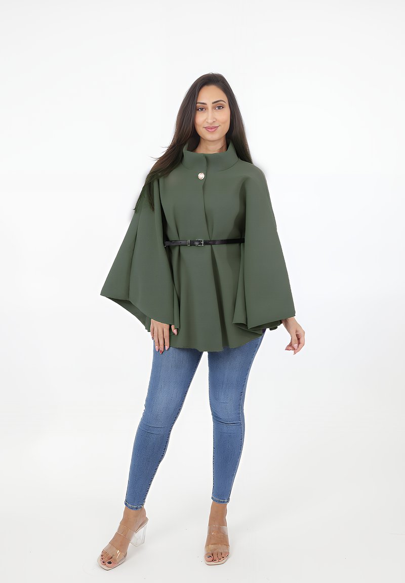 Grön kappa i texturerad tyg, med hög krage, framknäppning och ett svart bälte i midjan, kombinerad med blå slim fit-jeans och klara klackar.