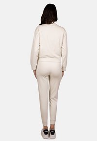 Felpa crema e pantaloni jogger coordinati, con polsini a coste e una vestibilità comoda, abbinati a sneakers bianche con accenti neri.