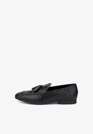 Mocassino slip-on in pelle intrecciata nera con nappine, suola piatta e tacco basso, mostrato in vista laterale su sfondo bianco.