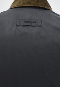 Dos de veste bleu foncé avec col en velours côtelé marron et patch logo Barbour cousu au centre supérieur.