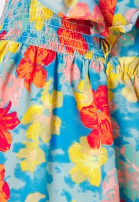 Tecido floral multicolorido com flores vibrantes em vermelho, rosa, amarelo e azul sobre um fundo azul claro com textura franzida.