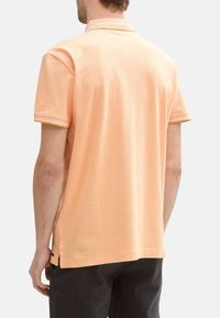 Polo en tissu doux pêche avec un col classique, des manches courtes et des rayures contrastées sur les poignets. Il possède des fentes sur les côtés à l'ourlet.