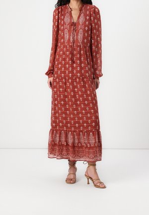 Langes, rostrotfarbenes Maxikleid mit stufigem Saum, langen Ärmeln und weißen Blumenmustern. Mit Bindeband am Ausschnitt und leichtem Stoff.