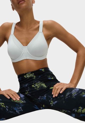Witte sportbeha met textuurpanelen, verstelbare bandjes en een naadloos ontwerp, gecombineerd met zwarte leggings met een kleurrijk abstract patroon.