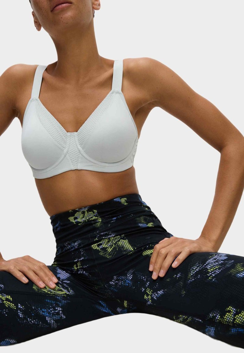 Reggiseno sportivo bianco con pannelli testurizzati, spalline regolabili e un design senza cuciture, abbinato a leggings neri con un motivo astratto colorato.