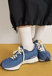Zapatillas deportivas azules con tejido texturizado, cordones blancos y una suela gruesa blanca. Llevadas con calcetas blancas de canalé y una prenda negra.