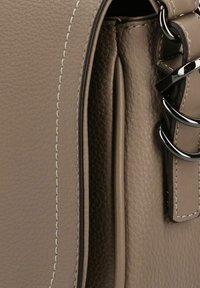 Beige Leder Tasche mit strukturiertem Oberflächen, ausgestattet mit kontrastierendem weißen Nähten und einem silbernen Hardware-Akzent an der Seite. Abgerundete Kanten.