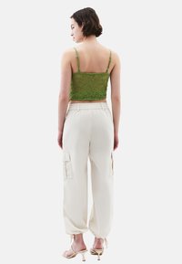 Zelený krajkový top na ramínka, doplněný volnými bílými cargo kalhotami s bočními kapsami a elastickými manžetami.