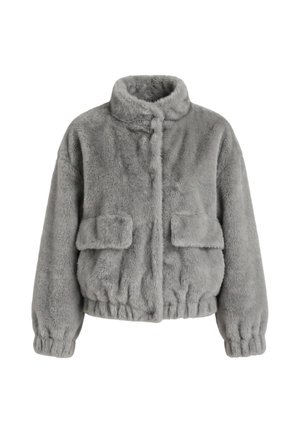 Femme portant une veste en fausse fourrure grise, un t-shirt blanc avec un motif Minnie Mouse, un pantalon cargo noir avec ceinture et des bottes noires, debout avec une main dans la poche.