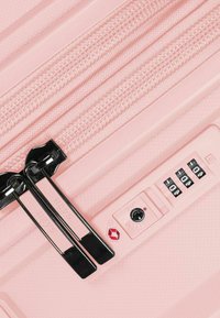 Maleta dura de color rosa claro con cremalleras a juego, un candado TSA y un mango retráctil con una superficie texturizada para un mejor agarre.